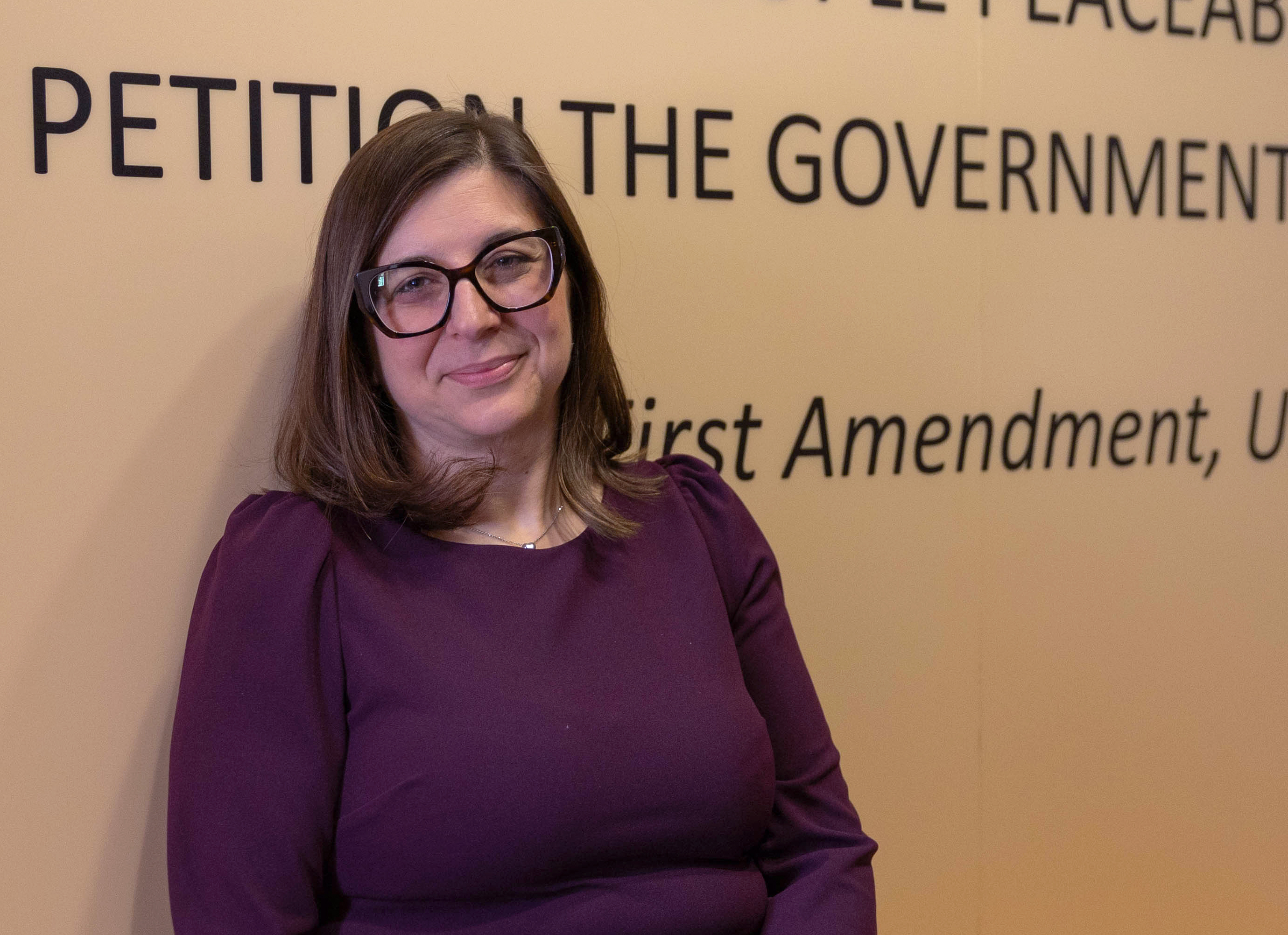 Elisia Cohen smiles next to wall text of the First Amendment