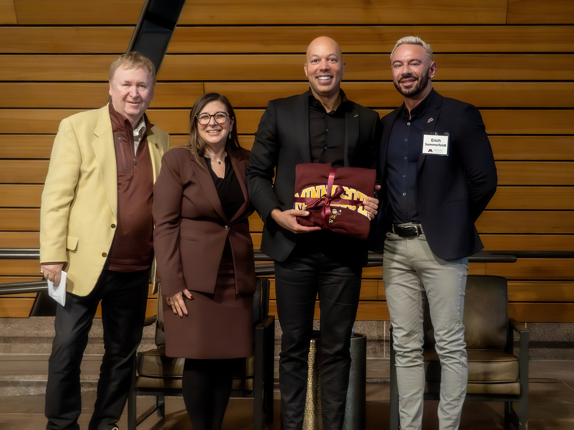 Four people pose smiling in a row